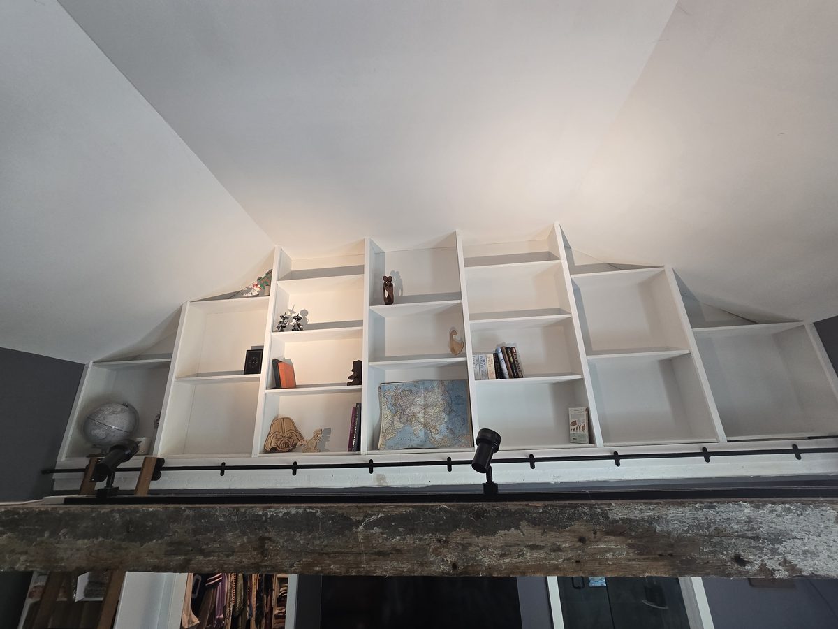 Custom built-in loft shelving, painted white, tucked under a vaulted ceiling